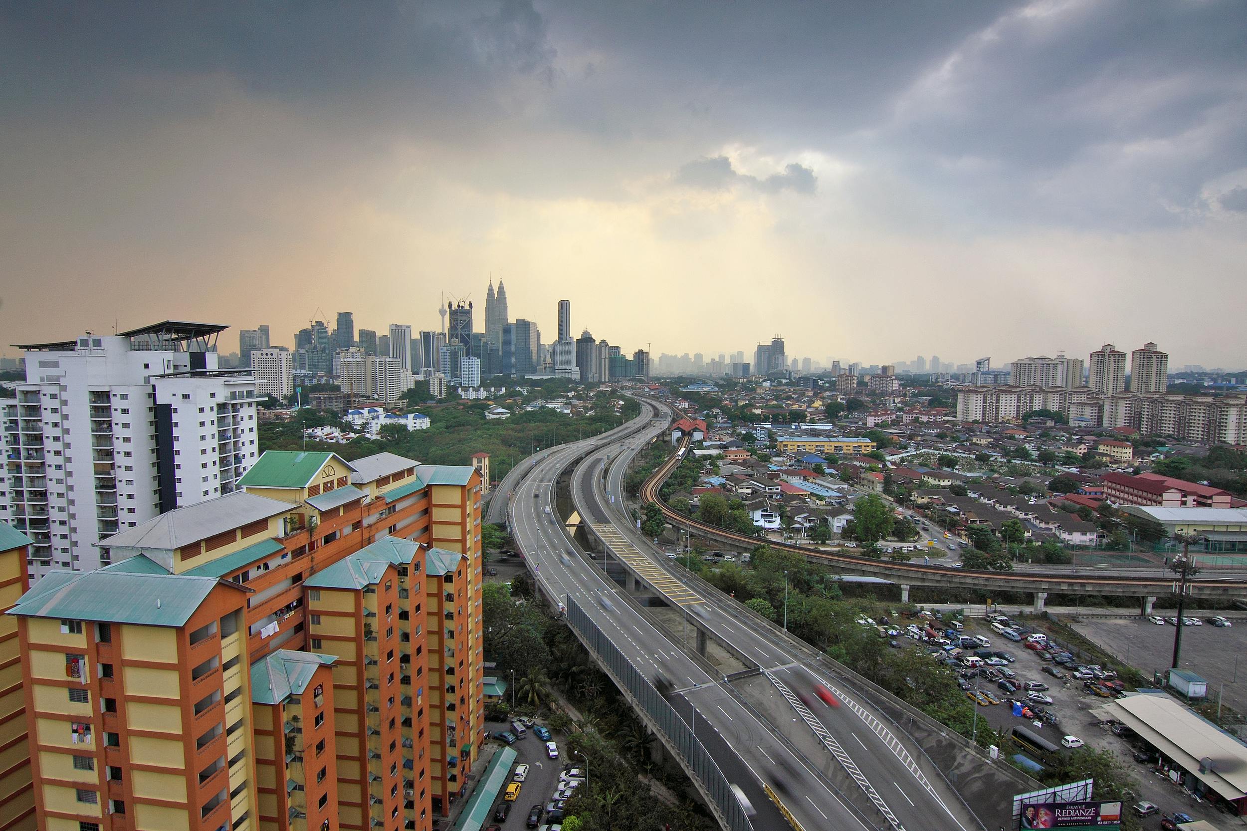 Aerial view of Kuala Lumpur skyline with modern buildings and highway at sunset.
